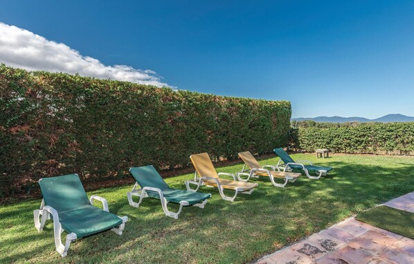 A row of outdoor lounge chairs aligned along a hedge, with a clear view of a vineyard and distant mountains. - Mas Girones: Rural con piscina (Riudellots)