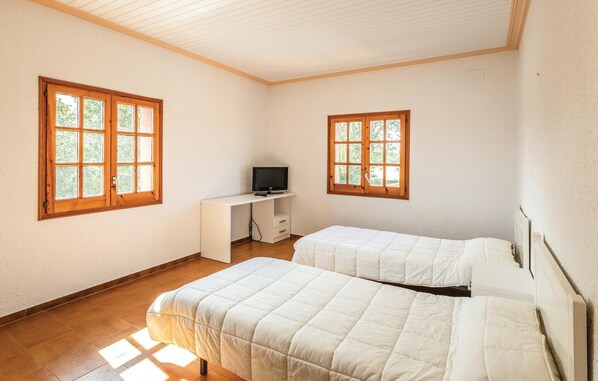 A room with two beds, a desk with a television, and large windows with wooden frames. - Mas Girones: Rural con piscina (Riudellots)