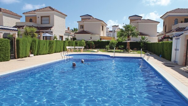 A swimming pool surrounded by houses with tiled roofs and manicured lawns.