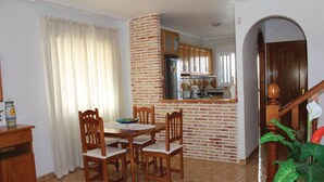 A dining area with a brick accent wall, wooden chairs, a table, and a kitchen in the background.