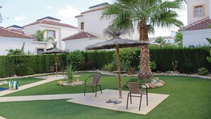 A well-maintained outdoor patio area with two wicker chairs, a thatched umbrella, and a palm tree.