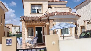 A two-story house with a tiled roof, a balcony, and a patio with chairs.