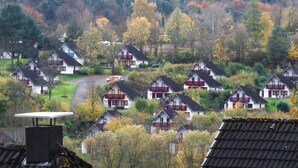 Ett bostadsområde med hus som har röda och vita fasader och som ligger i ett kuperat landskap med höstfärgat lövverk.