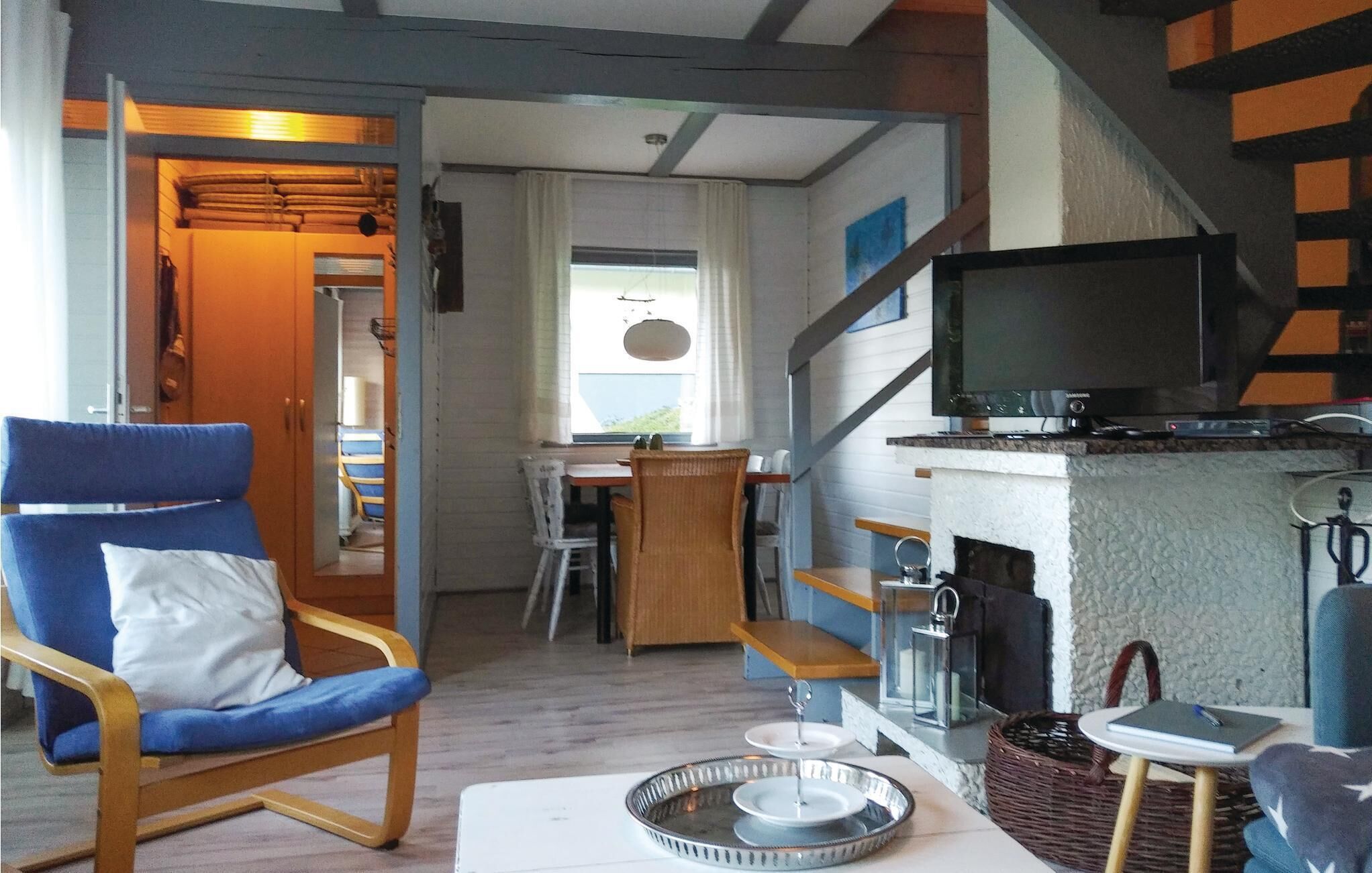 A cozy living room with a blue armchair, a television on a stone fireplace, and a dining area in the background.