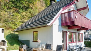 Ett litet hus med ett sluttande tak, en balkong med röda räcken och en uteplats med utemöbler.