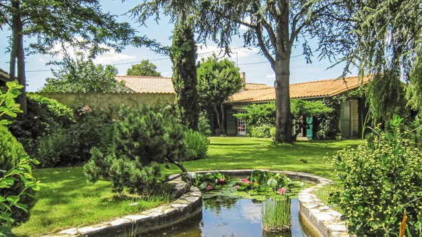 A serene garden with a pond, lush greenery, and a traditional building with a tiled roof. - Stunning home in Cézac (Cézac)