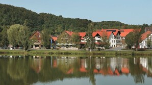 A lakeside view of traditional European-style buildings with red roofs, reflecting in calm water. - Room type A - Double room - Flair Hotel Werbetal (Waldeck)
