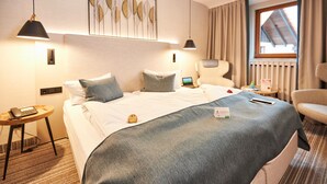 A hotel room with a neatly made bed, a desk with a computer, a chair, and a window with curtains. - Room type A - Double room - Flair Hotel Werbetal (Waldeck)