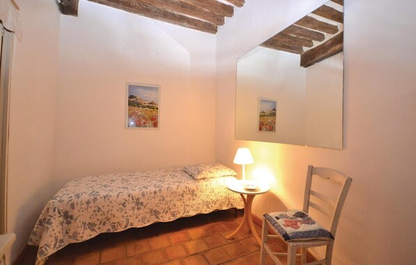 Une petite chambre à coucher avec un lit simple, une chaise, une table avec une lampe et deux tableaux encadrés accrochés au mur.