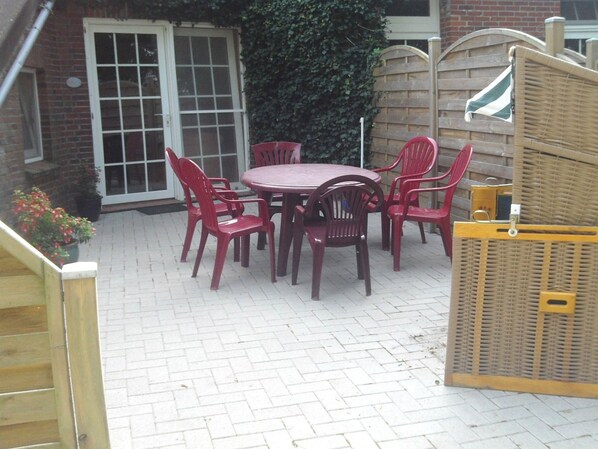 Eine Terrasse mit rundem Tisch und sechs Stühlen, umgeben von einer Ziegelmauer und einem Holzzaun.