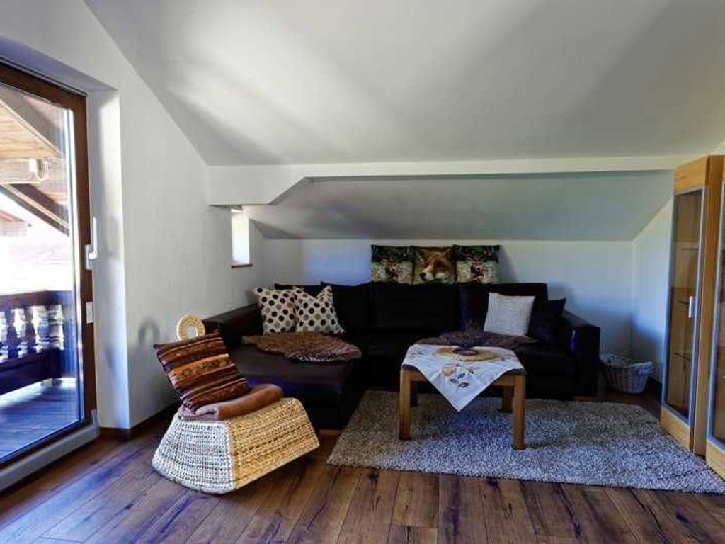 Ein gemütliches Wohnzimmer mit einer Couch, einem Korbstuhl, einem Couchtisch und einem gemusterten Teppich.