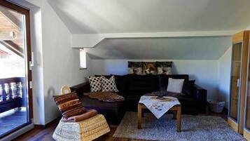 Ein gemütliches Wohnzimmer mit einer Couch, einem Korbstuhl, einem Couchtisch und einem gemusterten Teppich.