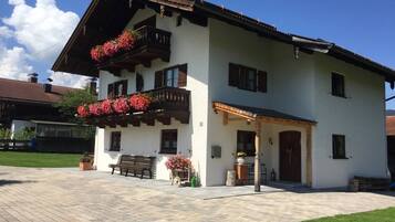 Ein zweistöckiges Gebäude mit einem Balkon, der mit roten Blumen, einer hölzernen Bank und einem gepflasterten Innenhof geschmückt ist.