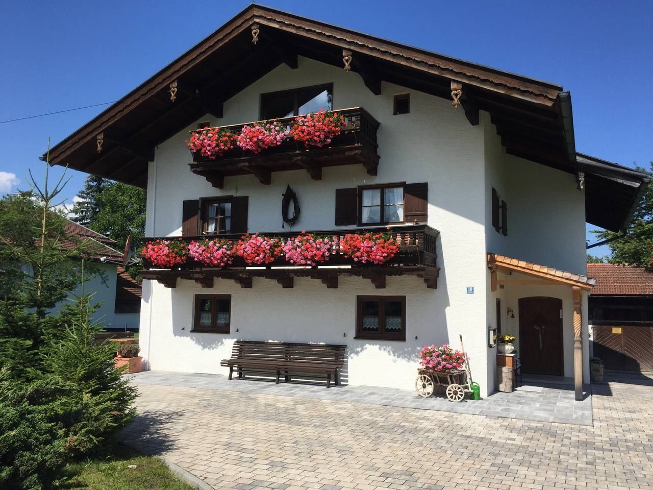 Ein zweistöckiges Gebäude mit einem Balkon, der mit roten Blumen, einer hölzernen Bank und einem gepflasterten Eingangsbereich verziert ist.