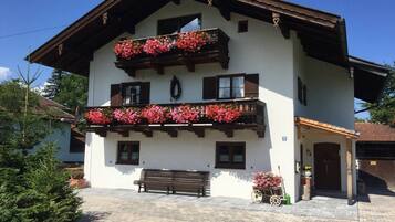 Ein zweistöckiges Gebäude mit einem Balkon, der mit roten Blumen, einer hölzernen Bank und einem gepflasterten Eingangsbereich verziert ist.