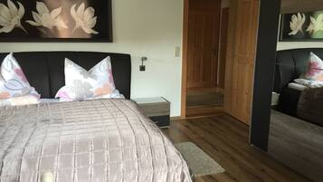 Ein Schlafzimmer mit einem großen Bett, Holzboden, einem Nachttisch und einer Tür zu einem weiteren Raum.