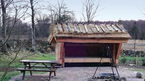 A rustic wooden structure with a thatched roof, a wooden bench, and a fire pit. - Stunning home in Linderöd with WiFi (Linderöd)