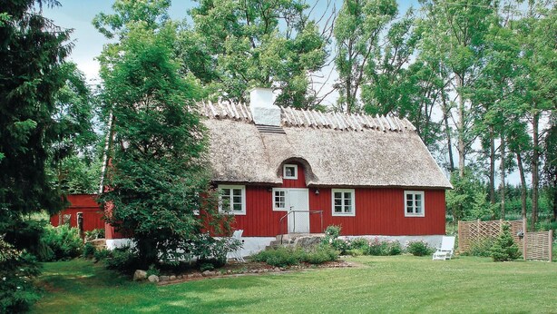 A red wooden house with a thatched roof, surrounded by a lush green garden and tall trees. - Stunning home in Linderöd with WiFi (Linderöd)