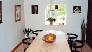 A dining area with a long wooden table, four chairs, a hanging light fixture, and a window with a plant. - Stunning home in Linderöd with WiFi (Linderöd)