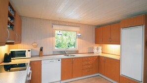 A compact kitchen with wooden cabinets, a white dishwasher, a microwave, a sink, and a refrigerator. - 5 bedroom amazing home in Væggerløse (Væggerløse)