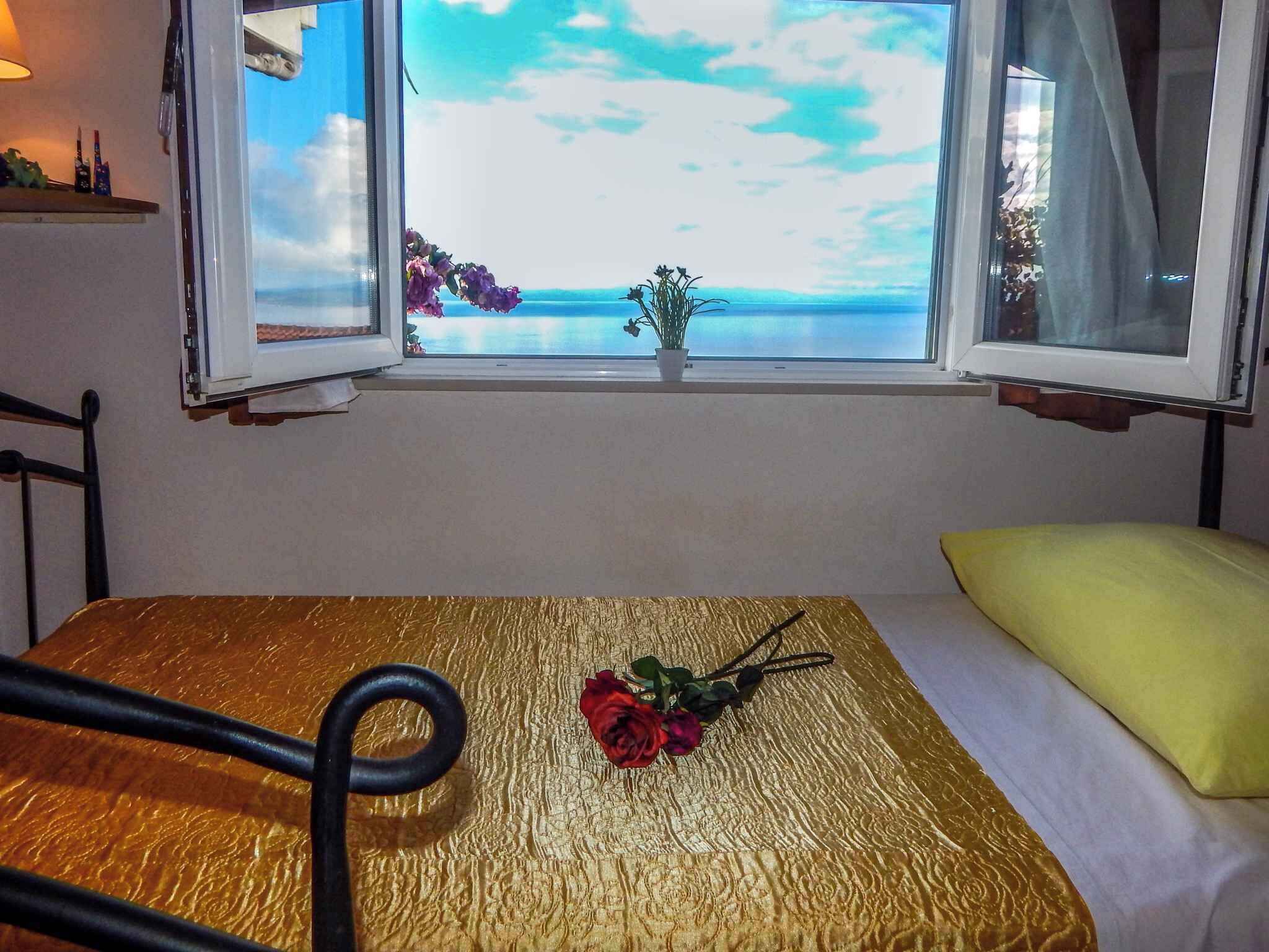 Um quarto com cama, uma mesa com uma rosa e uma janela com vista para o mar.