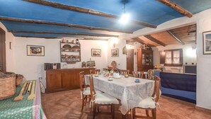 Un coin repas avec une table dressée pour quatre personnes, entourée de chaises en bois. Un buffet en bois avec des portes en verre se trouve à gauche, et un canapé bleu est visible au fond.