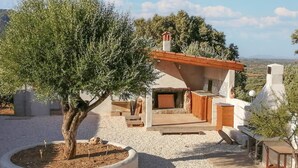 Une cuisine extérieure rustique, dotée d’un four en pierre, entourée de gravier et d’un grand arbre.