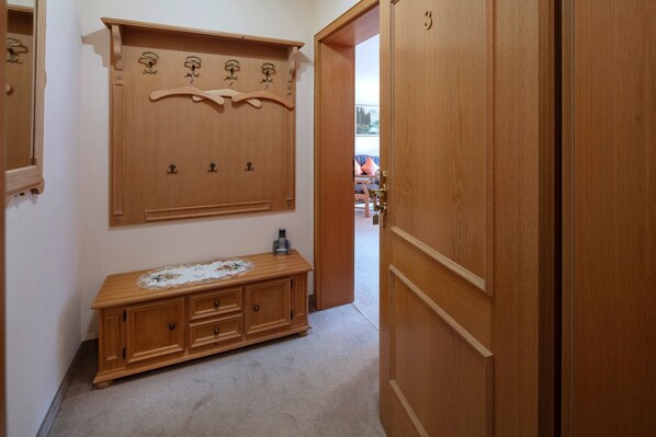 Een gang met een houten garderobe, een houten dressoir en een deur met een nummer.