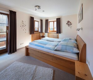 Een slaapkamer met een houten bed, twee raamdecoratie met gordijnen, een radiator en een wandlamp.