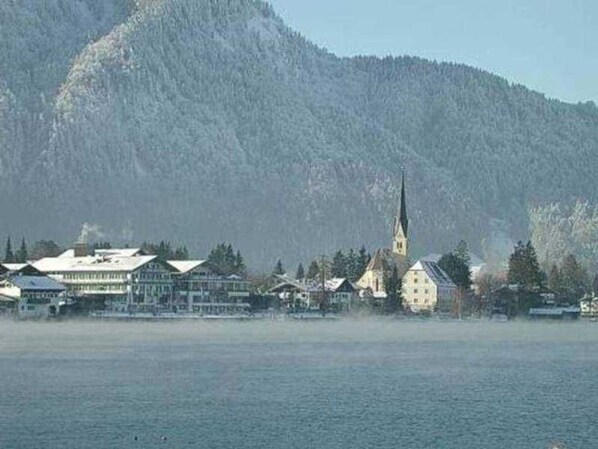 A lakeside town with a prominent church steeple, buildings with sloped roofs, and a mountainous backdrop. - Apartment 3 - Apartments Lohbinder (Fam. Holzer) (Rottach-Egern)