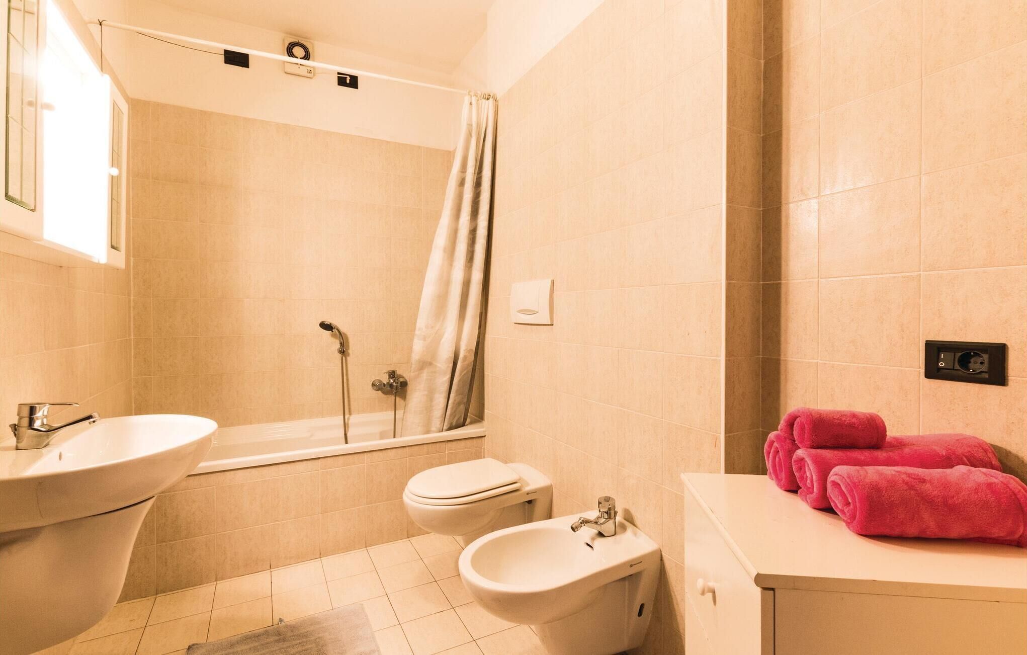 A bathroom with a bathtub, a toilet, a bidet, and a sink. There are pink towels on the counter.