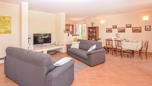 Ein Wohnzimmer mit zwei grauen Sofas, einem Fernseher, einem Essbereich mit Tisch und Stühlen sowie einer Küchenzeile mit Schränken und einem Fenster.