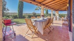 Ein Essbereich im Freien mit überdachter Terrasse, Holzstühlen, einem Tisch für zwei Personen und einem roten Grillwagen.
