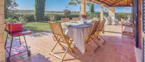 Ein Essbereich im Freien mit überdachter Terrasse, Holzstühlen, einem Tisch für zwei Personen und einem roten Grillwagen.