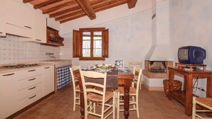 Una cuina rústica amb bigues de fusta, una taula de menjador preparada per a quatre persones i una televisió antiga sobre un suport de fusta.