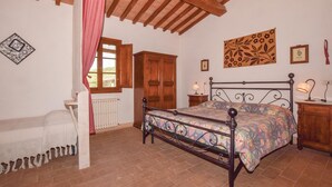 Un dormitori amb sostre de fusta, un llit amb edredó estampat, un radiador, una finestra amb cortines i un armari de fusta.