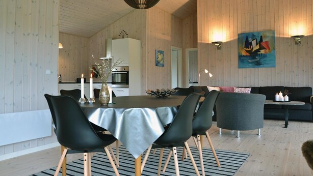 A modern dining area with a table set for four, surrounded by black chairs with wooden legs. A vase with flowers and candles are on the table. - Cozy home in Jægerspris with WiFi (Jægerspris)