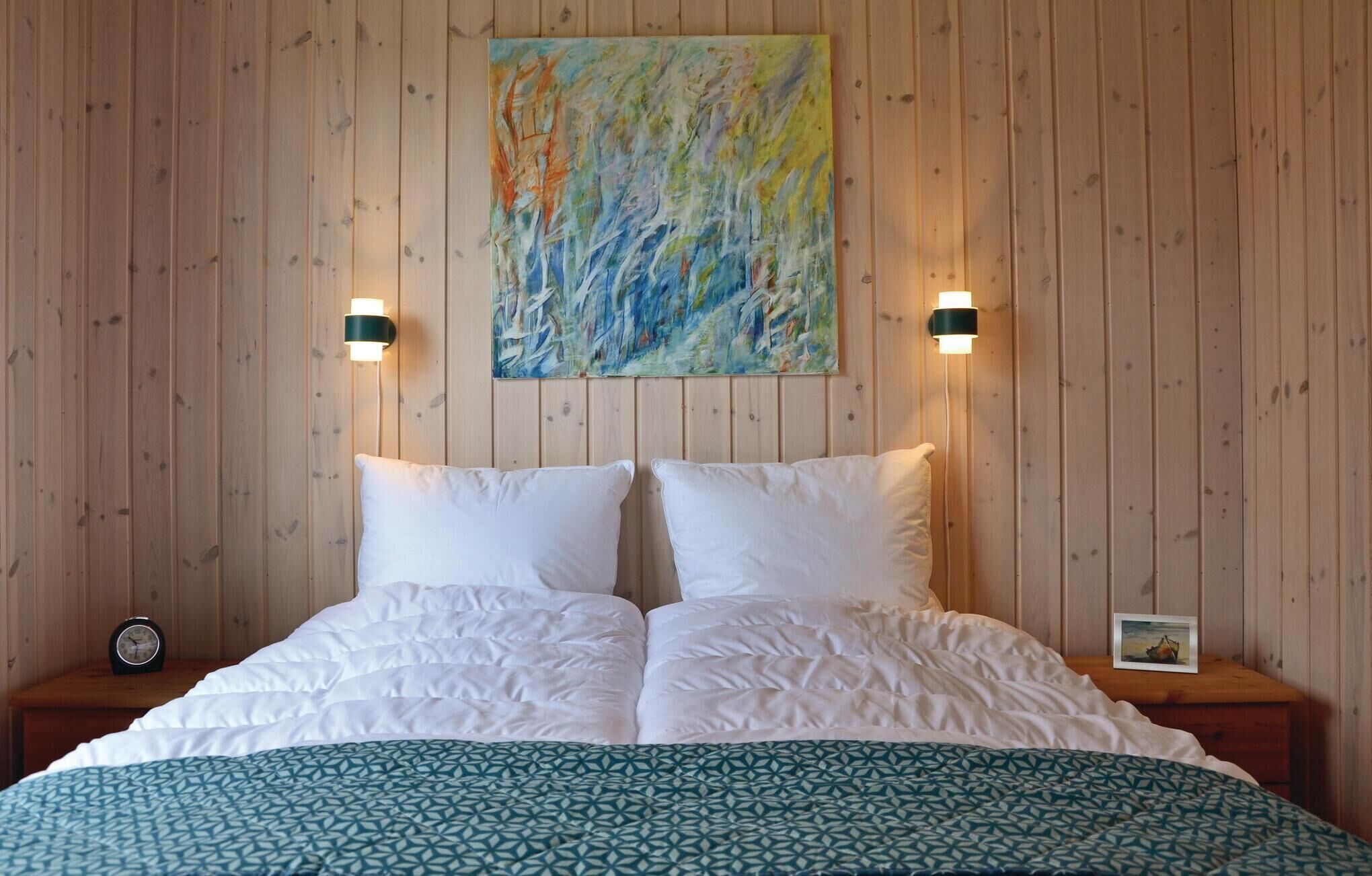 Une chambre d’hôtel avec un mur lambrissé en bois, un grand lit avec une literie blanche, deux lampes de chevet et un tableau au-dessus du lit.
