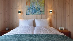 A hotel room with a wooden paneled wall, a large bed with white bedding, two bedside lamps, and a painting above the bed. - Cozy home in Jægerspris with WiFi (Jægerspris)