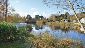 A serene lakeside setting with a house and a greenhouse in the background. - Cozy home in Jægerspris with WiFi (Jægerspris)
