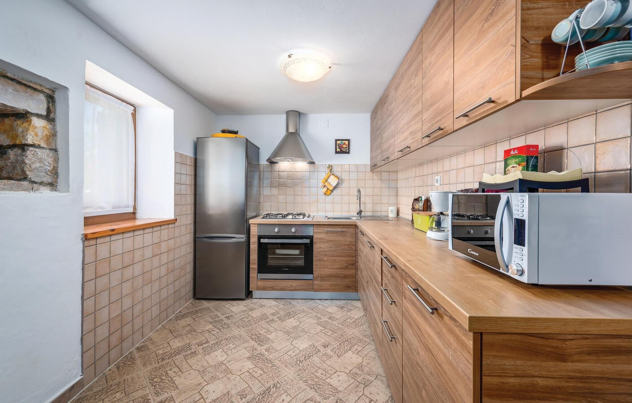 Une cuisine de taille réduite équipée d’un réfrigérateur, d’un four, d’un four à micro-ondes et de meubles de rangement en bois.