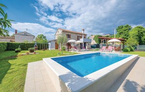 Ein Swimmingpool mit Liegestühlen und Sonnenschirmen, umgeben von einer gepflegten Rasenfläche und Steingebäuden.
