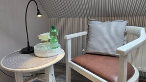 A white chair with a brown cushion, a small round table with a lamp, a bottle, and a glass container with a flower. - Single Room - Pension Max (Senftenberg)