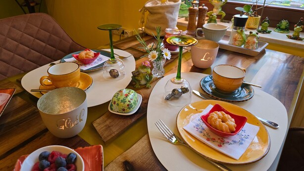 A dining table set with various dishes, a coffee cup, and a decorative frog figurine. - Single Room - Pension Max (Senftenberg)