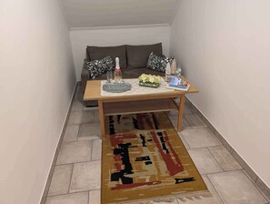 Una sala pequeña con un sofá, una mesa de centro de madera, una alfombra y algunos objetos decorativos.