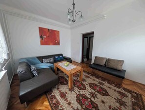 Una sala de estar con un sofá de cuero negro, una mesa de centro de madera y un tapete estampado.