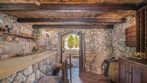 A rustic stone-walled kitchen with a wooden bench, a stone archway, and a wooden cabinet.