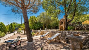 A patio with two lounge chairs, a stone wall, and a small brick structure.
