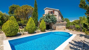 A swimming pool with a stone deck, surrounded by various trees and a stone building with a balcony.