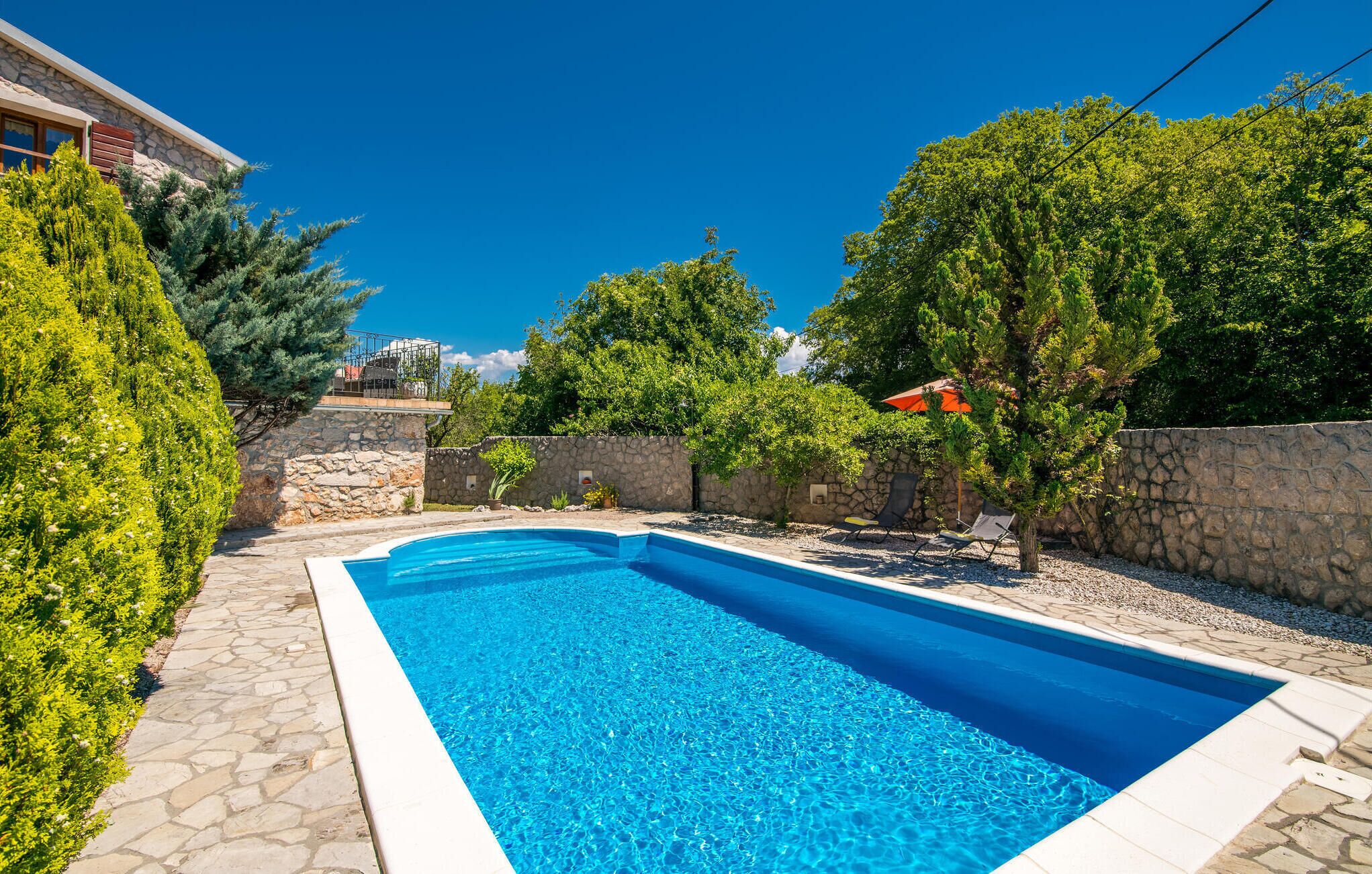 Une piscine aux bords recouverts de pierres, entourée de verdure et de murs en pierre.